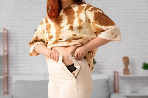 Image of woman trying to do her trousers up after pregnancy weight gain Cheltenham