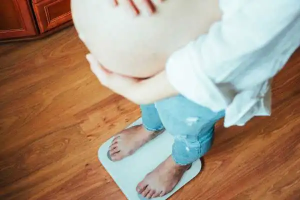 Image of woman weighing herself and experiencing weight gain through pregnancy Cheltenham